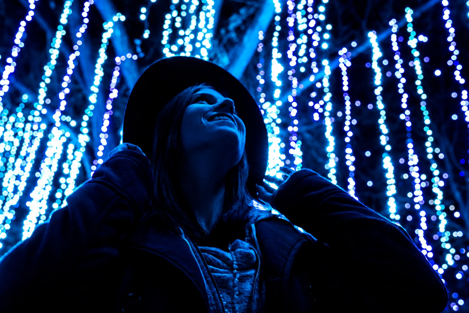A smiling woman in a dark hat surrounded by glowing blue lights at night.